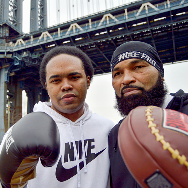 Two black males pose wearing boxing gloves under bridge in New York